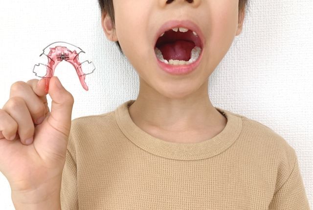 口を開けて手に持つ矯正装置を見せる男の子