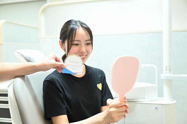 シェードガイドと歯を見せて笑う女性